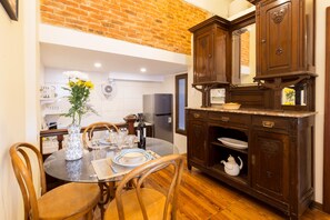 A dining area with a round glass table, wooden chairs, and a dark wooden cabinet with a mirror. - The Wall Montevideo [001] Studio in the Old Town (Montevideo)
