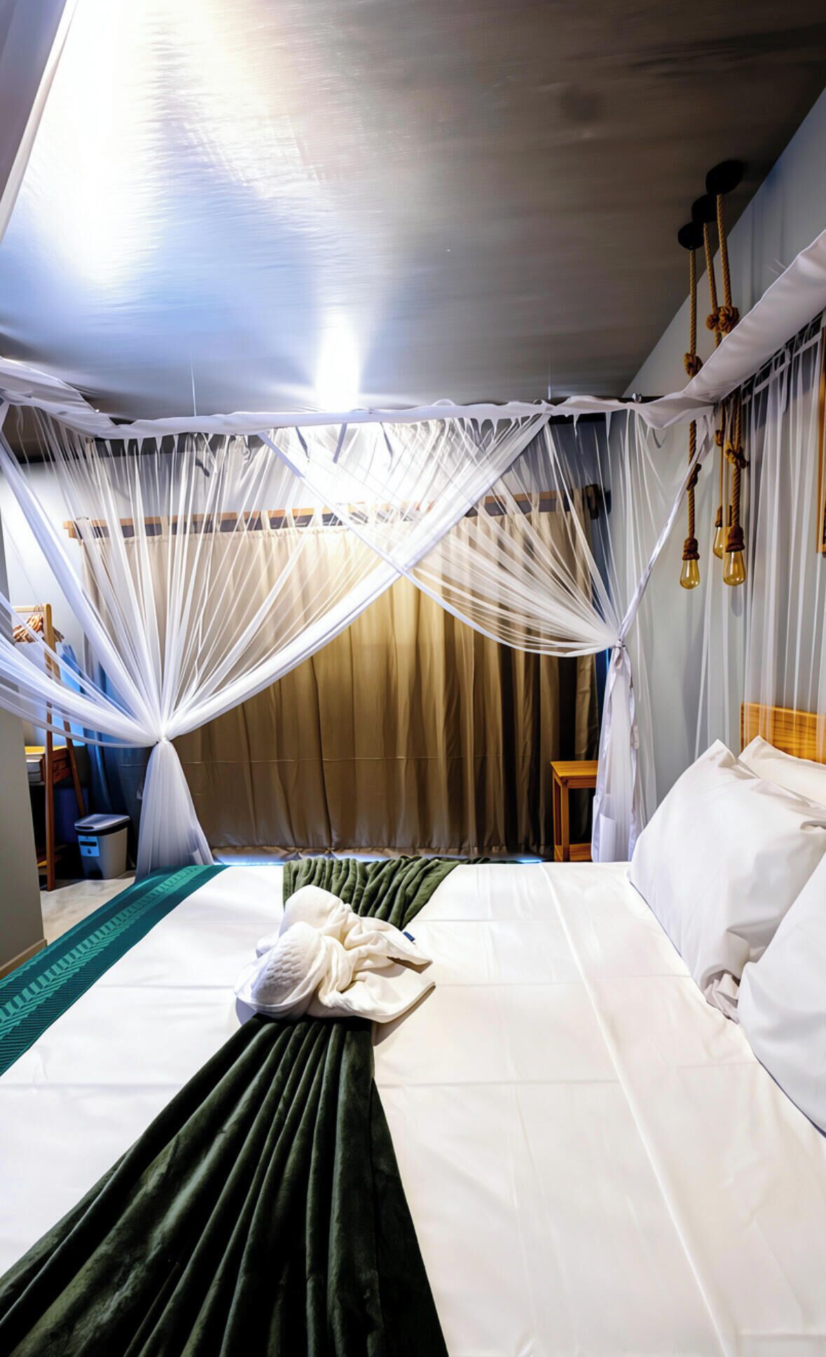A hotel room with a bed, a green throw, a white canopy, and a wooden headboard.