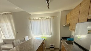 A modern kitchen with granite countertops, wooden cabinets, a stainless steel refrigerator, and a built-in island with seating. - Pleasant 2-bedroom apartment with AC in Punta Cana (Punta Cana)