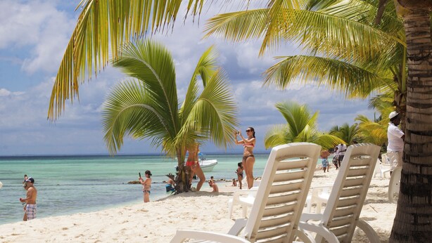 A beach with white lounge chairs, palm trees, and people enjoying the water. - Pleasant 2-bedroom apartment with AC in Punta Cana (Punta Cana)