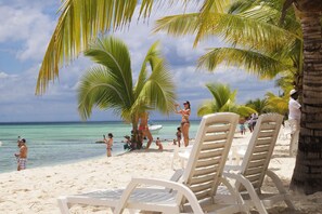 A beach with white lounge chairs, palm trees, and people enjoying the water. - Pleasant 2-bedroom apartment with AC in Punta Cana (Punta Cana)