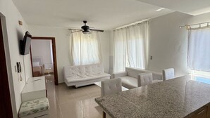 A modern kitchen with a granite countertop and wooden cabinets, a white sofa, and a ceiling fan. - Pleasant 2-bedroom apartment with AC in Punta Cana (Punta Cana)