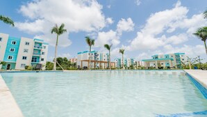 A swimming pool with clear water, surrounded by multi-story buildings with balconies and palm trees. - Pleasant 2-bedroom apartment with AC in Punta Cana (Punta Cana)