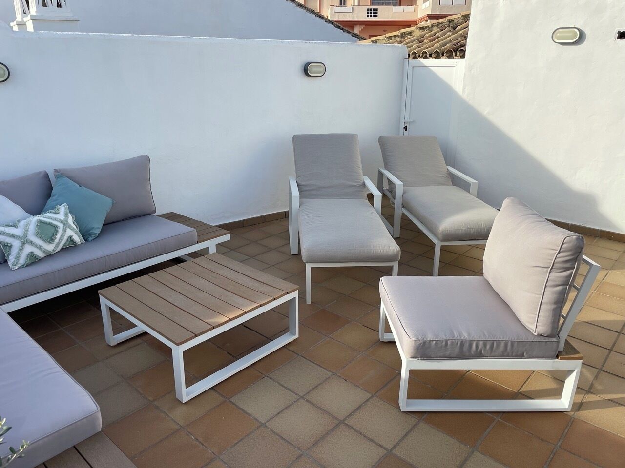 Eine Dachterrasse mit einer Couch, zwei Sesseln, einer Bank und einem Holztisch.