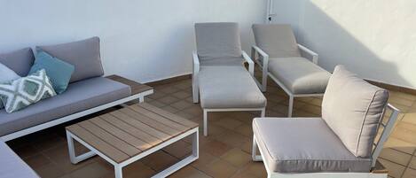 Eine Dachterrasse mit einer Couch, zwei Sesseln, einer Bank und einem Holztisch.
