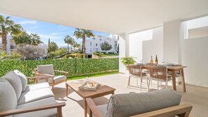 A modern outdoor patio with a sofa, chairs, and a dining table set for two. - Stylish 2-pax Stay in Alcazaba Lagoon (Casares)