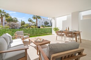 Eine moderne Terrassenanlage mit einer Couch, Sesseln und einem Esstisch für zwei Personen.