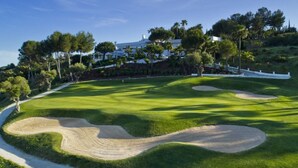 A golf course with bunkers, a white building, and trees. - Stylish 2-pax Stay in Alcazaba Lagoon (Casares)