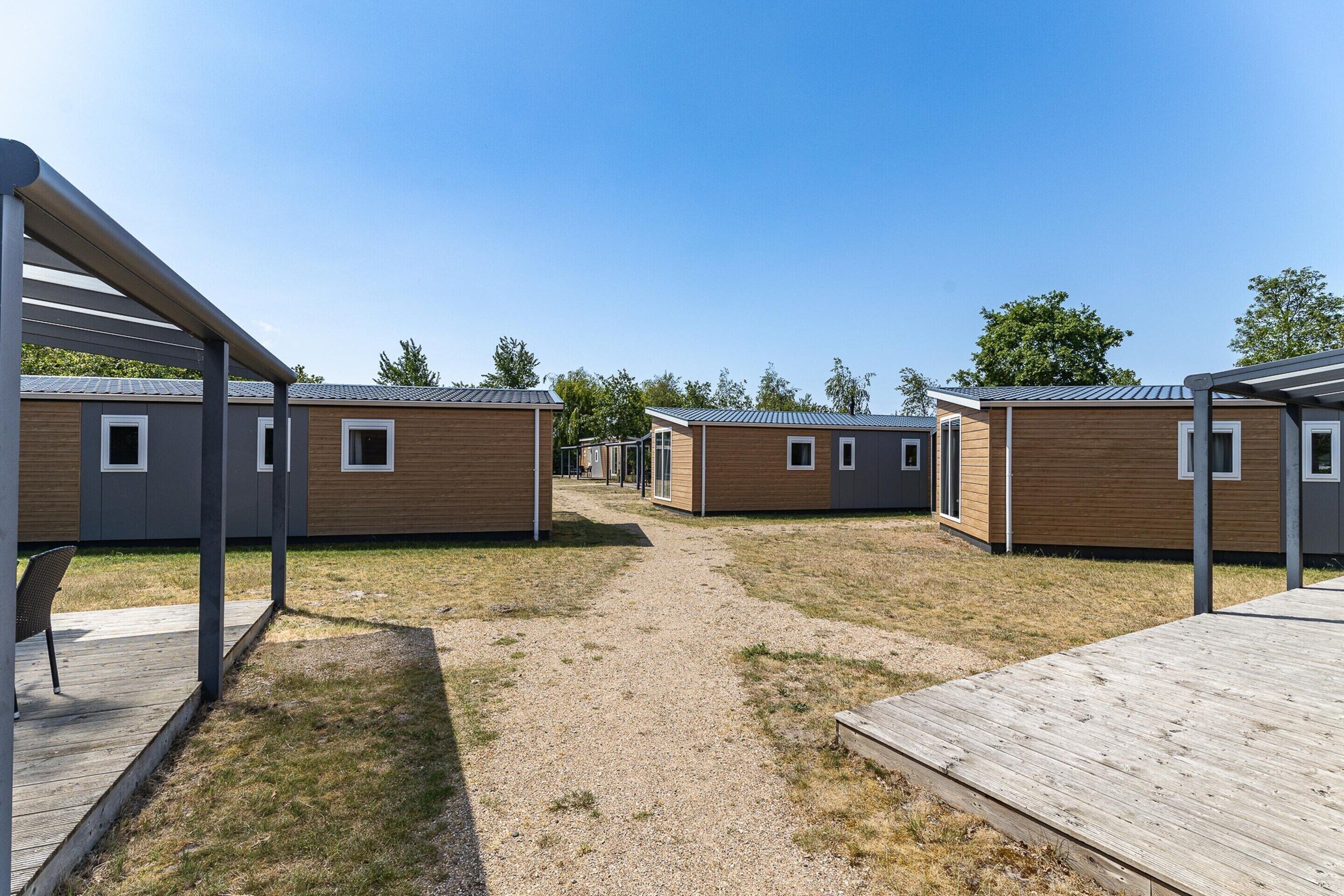 A row of modern, compact cabins with a gravel path between them, wooden decks, and a clear blue sky.