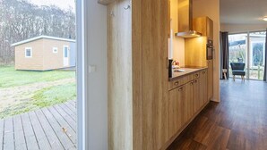 A modern kitchen with wooden cabinets, a built-in oven, and a large window overlooking a backyard. - Cosy Family Chalet With Covered Terrace (Burgh-Haamstede)