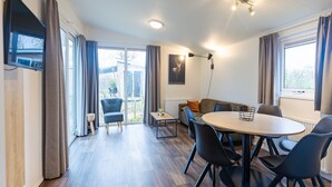A modern room with a round table, chairs, a sofa, and a television. - Cosy Family Chalet With Covered Terrace (Burgh-Haamstede)