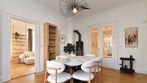 Un coin repas comprenant une table ronde, six chaises, un poêle noir et une bibliothèque en bois.
