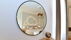 Une chambre à coucher avec un miroir rond, un lit surmonté d’un luminaire en forme de nuage et un globe posé sur une table de chevet en bois.