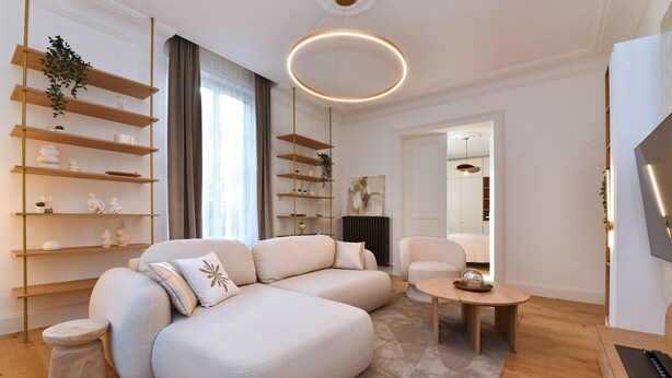Un salon moderne avec un canapé d’angle, des étagères en bois, une table basse ronde et un téléviseur à écran plat.
