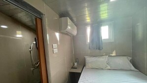 A hotel room with a bed, a window with curtains, an air conditioning unit, and a shower area. - Charinsup Pinklao hotel (Bang Kruai)