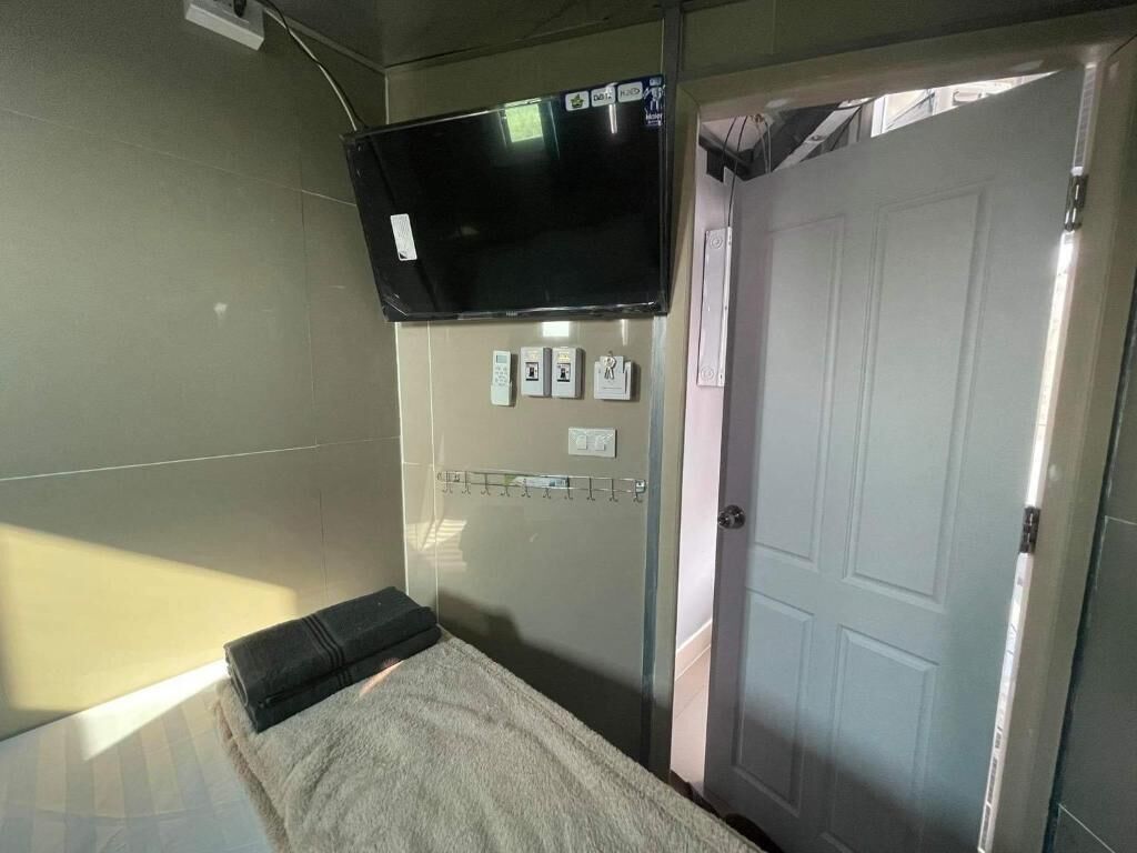 A room with a bed, a television mounted on the wall, a door, and a light switch panel.