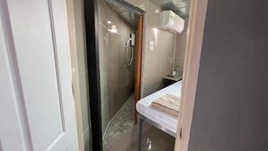 A bathroom with a glass shower enclosure, a towel on the floor, and a white air conditioning unit on the wall. - Charinsup Pinklao hotel (Bang Kruai)