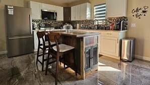 Une cuisine dotée d’un îlot central, de tabourets de bar, d’un réfrigérateur, d’un four à micro-ondes et d’une enseigne indiquant l’emplacement du coin café.