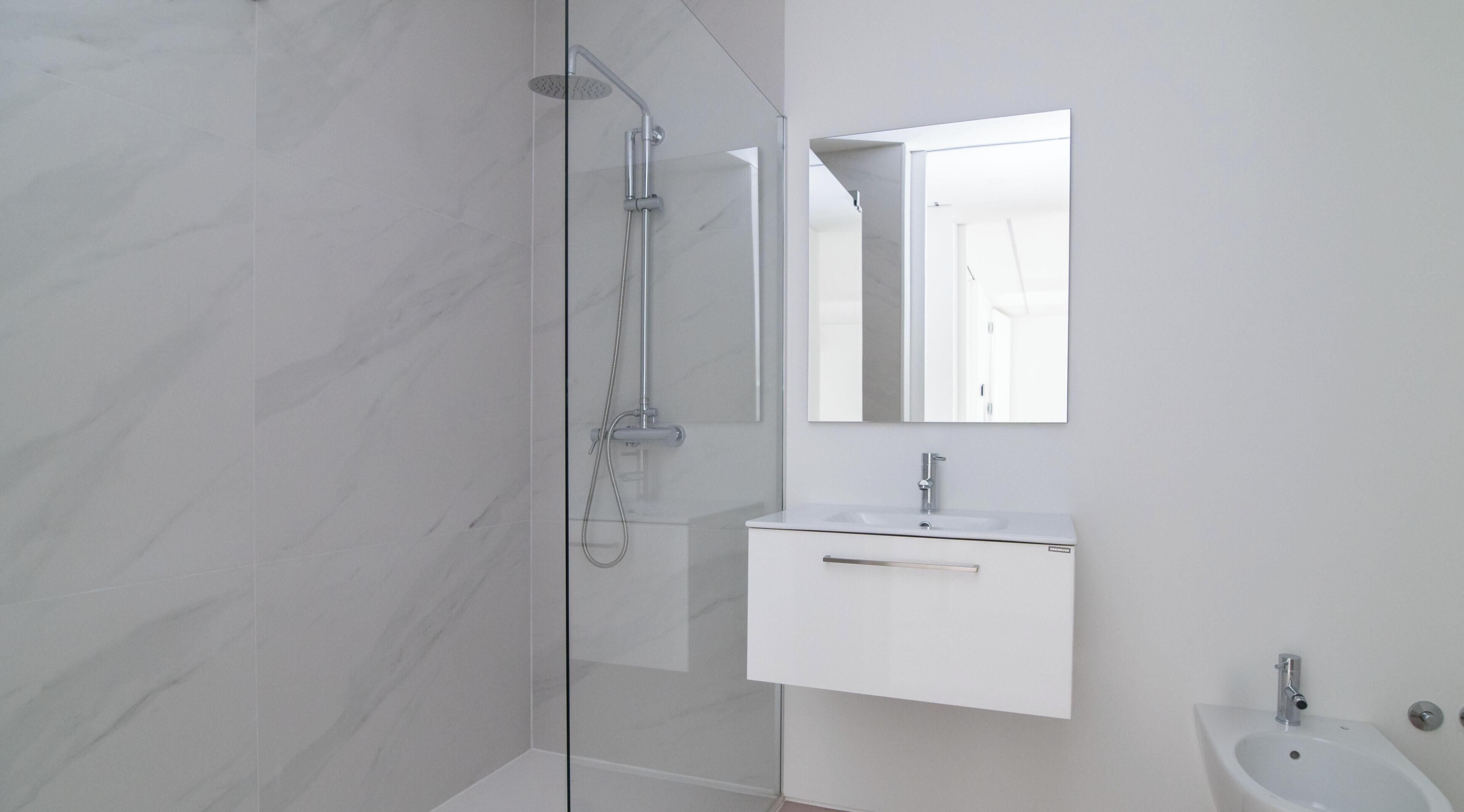 A modern bathroom with a glass-enclosed shower, a white sink, and a mirror above it.