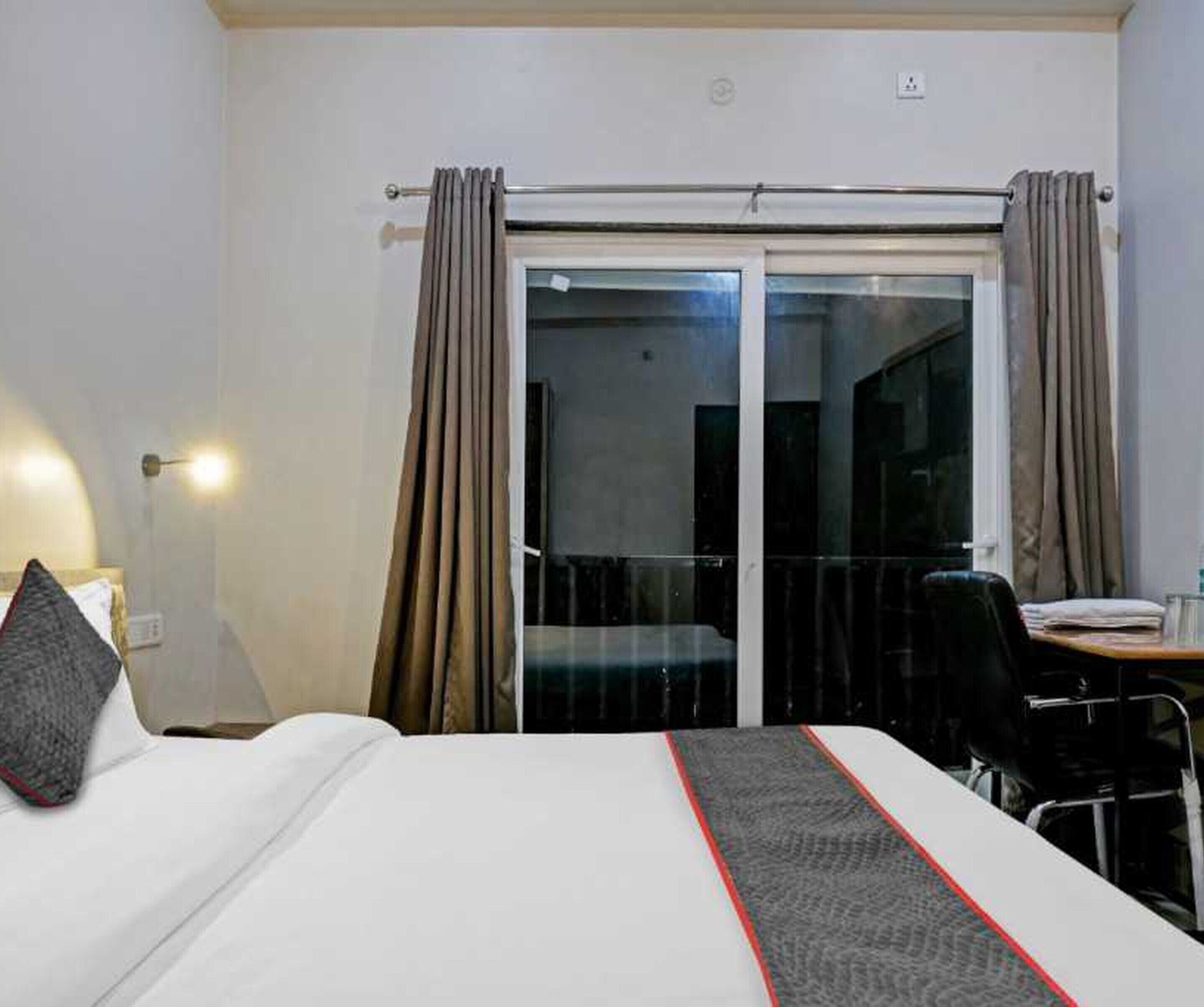 A hotel room with a bed, a desk, a chair, and a sliding glass door leading to a balcony.