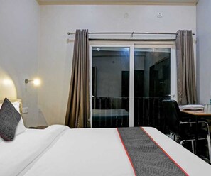 A hotel room with a bed, a desk, a chair, and a sliding glass door leading to a balcony.