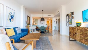 A modern living room with a blue sofa, wooden coffee table, and a dining area with a round table and chairs. - Benahavis Abode With Panoramic Views (Benahavis)