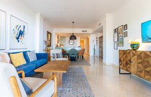A modern living room with a blue sofa, wooden coffee table, and a dining area with a round table and chairs. - Benahavis Abode With Panoramic Views (Benahavis)