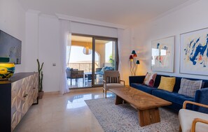 Una sala de estar moderna con un sofá azul, una mesa de centro de madera y un comedor con puerta de vidrio que da a un patio exterior.