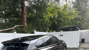 Un Toyota Land Cruiser LS7 noir est garé sur une allée de gravier, avec une clôture blanche et des arbres en arrière-plan.