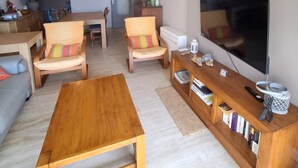 A living room with a wooden coffee table, two armchairs, a sofa, a flat-screen TV, and a bookshelf. - Well-located apartment with beautiful sea view. (Saint-Raphaël)
