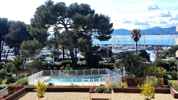 A pool surrounded by a white fence, with a view of a marina and boats in the background. - Well-located apartment with beautiful sea view. (Saint-Raphaël)