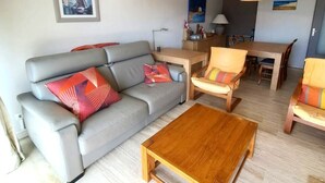 A living room with a grey sofa, wooden coffee table, and two armchairs. There is a dining table with chairs and a lamp. - Well-located apartment with beautiful sea view. (Saint-Raphaël)