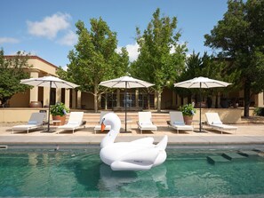 Área de piscina com espreguiçadeiras, guarda-sóis e um flutuador em formato de cisne.