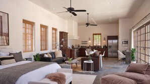 A spacious living area with a large bed, a sofa, a coffee table, and a dining table. There is a kitchen in the background with a refrigerator and a microwave. - The Ridge: A Secluded Luxury Estate with Pool (Santa Fe)