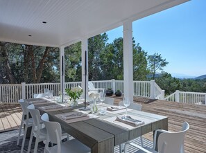 Een terras met een houten dek, witte stoelen en een tafel gedekt voor een maaltijd.