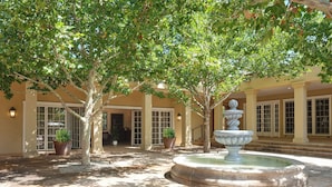 A courtyard with a fountain, trees, and a building with large windows and doors. - The Ridge: A Secluded Luxury Estate with Pool (Santa Fe)