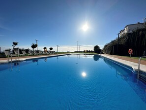 A clear blue swimming pool with metal ladders, sun, and a building in the background. - Scenic Sea, Mountain & City View Holiday Apartment (Manilva)