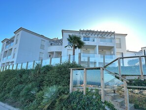 A multi-story residential building with balconies, a palm tree, and a glass structure in the foreground. - Scenic Sea, Mountain & City View Holiday Apartment (Manilva)