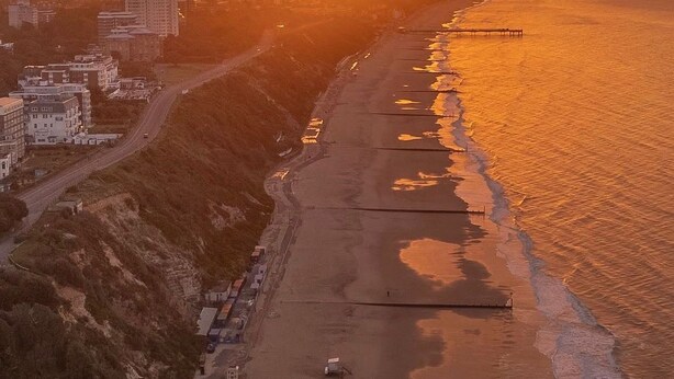 An aerial view of a coastal area during sunset with buildings along the shore and a pier extending into the water. - Cosy 2 bed retreat 10 mins to airport/beach/city ctr!  5 mins to train station (Bournemouth)