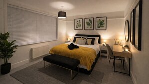A bedroom with a bed, bedside tables, a desk, a potted plant, and framed pictures on the wall. - Cosy 2 bed retreat 10 mins to airport/beach/city ctr!  5 mins to train station (Bournemouth)