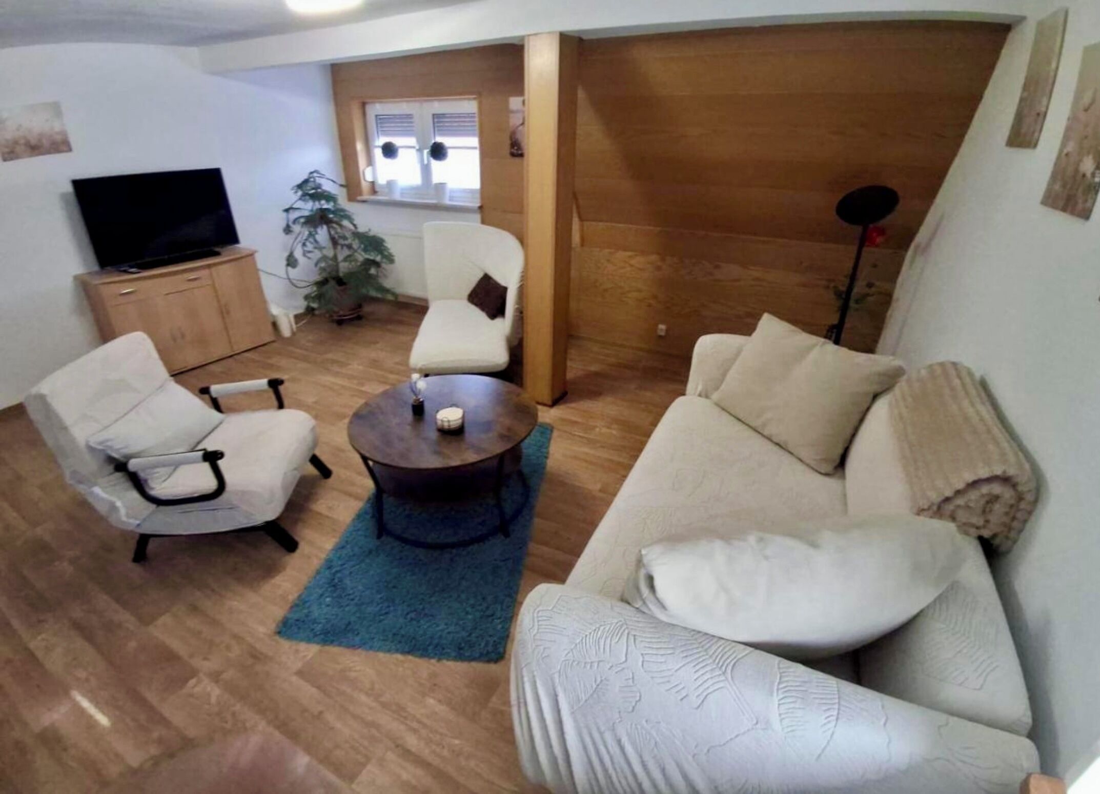 A living room with a sofa, armchairs, a coffee table, a TV, and a wooden cabinet.