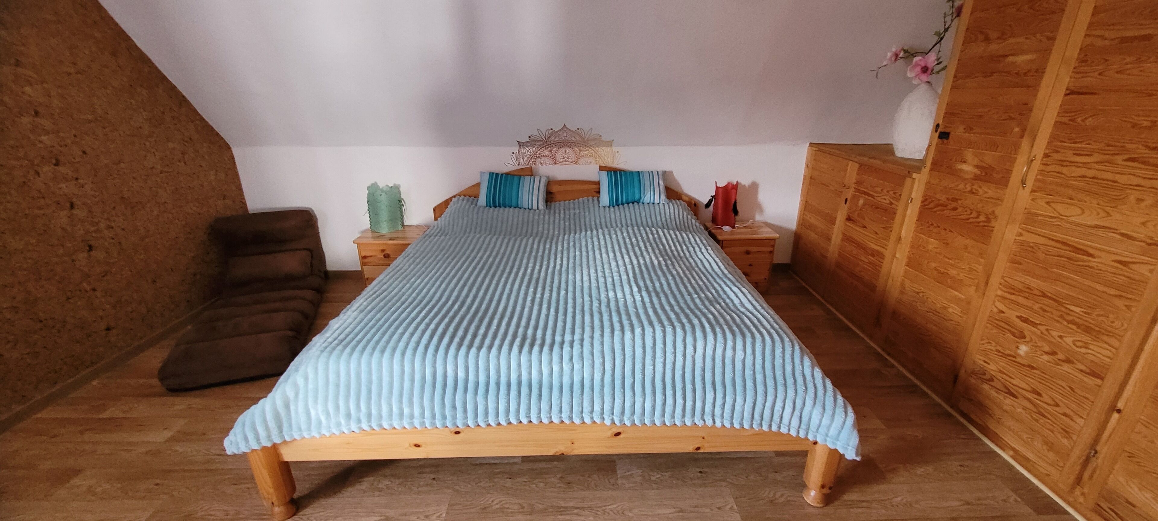 A bedroom with a wooden bed, a nightstand, a chair, and a wooden wardrobe.
