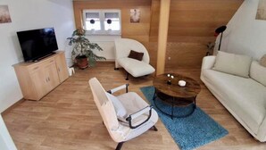 Una sala de estar con televisor, sofá, sillón, mesa de centro y planta.