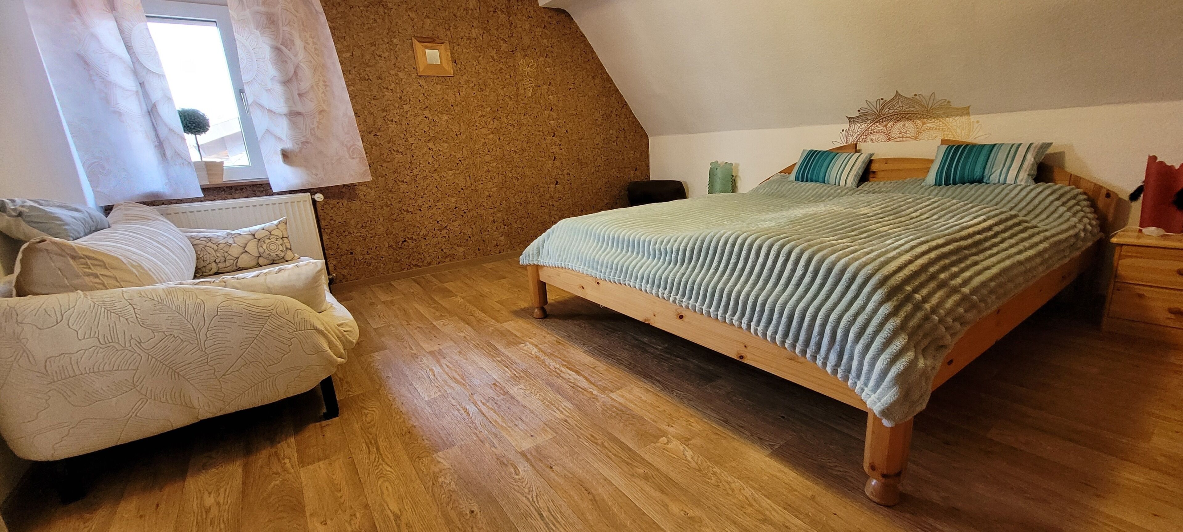 A bedroom with a wooden bed, a chair, a small table, and a window with curtains.