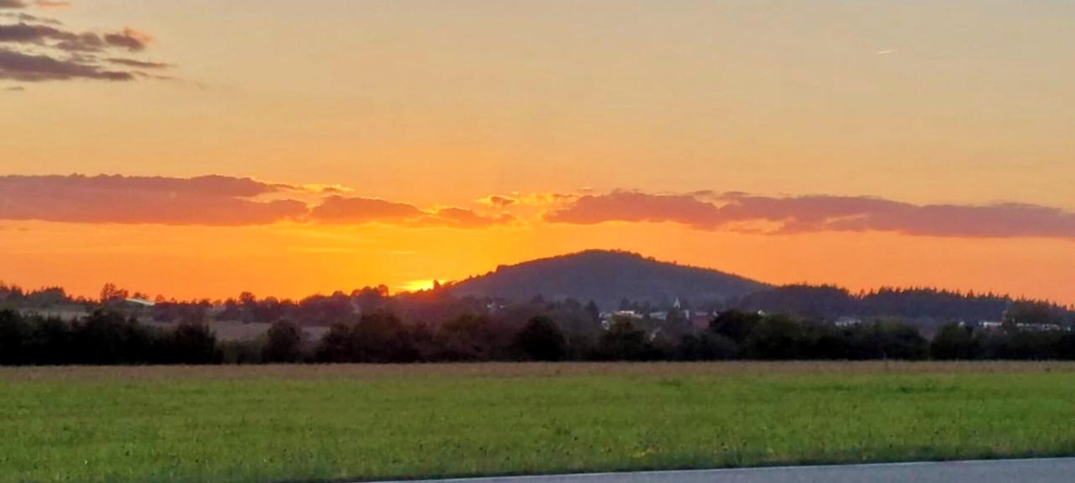Un atardecer sobre un campo verde con una colina al fondo.