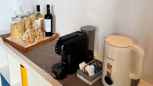 Un comptoir dans une chambre d’hôtel avec une machine à café, une tasse, des en-cas et des bouteilles de vin.