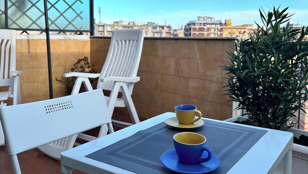 Une terrasse sur le toit avec une table dressée pour deux personnes, deux chaises, un grand parasol et des guirlandes lumineuses.
