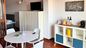 Une pièce moderne avec une table ronde, des chaises blanches, un meuble blanc et un téléviseur à écran plat fixé au mur.