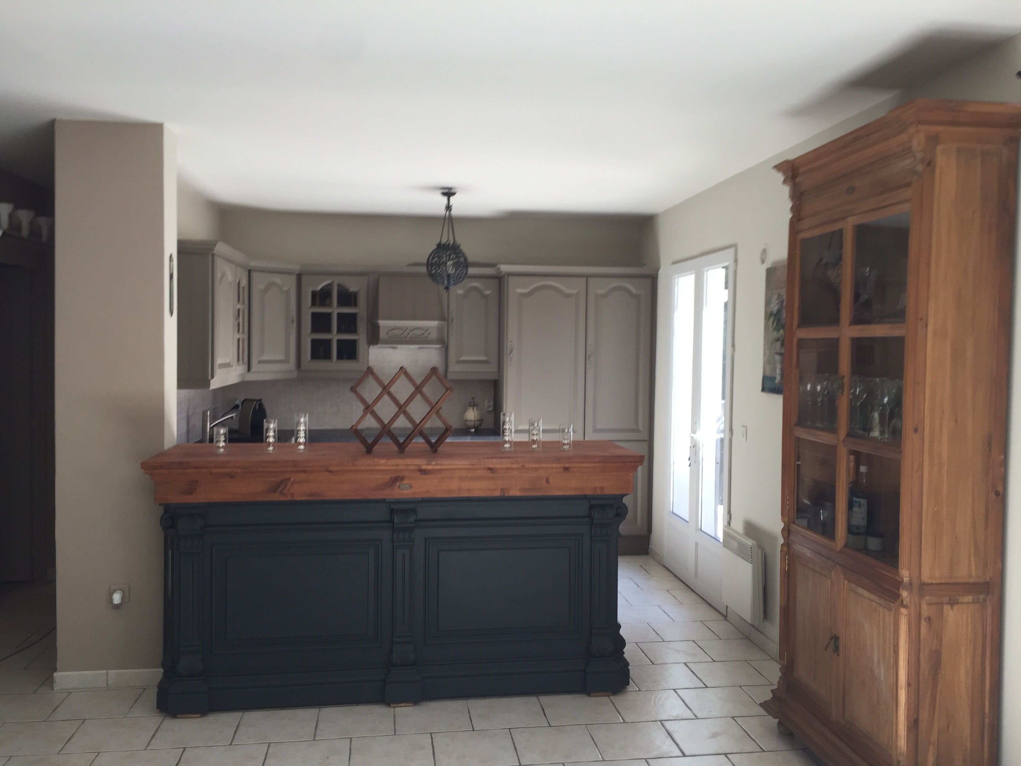 Une cuisine dotée d’un îlot central, de meubles blancs et d’un meuble en bois avec des portes en verre.