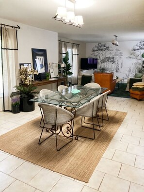 A dining area with a glass table and wicker chairs, a sofa, a television, and a mural on the wall. - AIR-CONDITIONED PROVENCAL HOUSE WITH POOL AND SPA ON THE ROAD TO BIOT (Antibes)